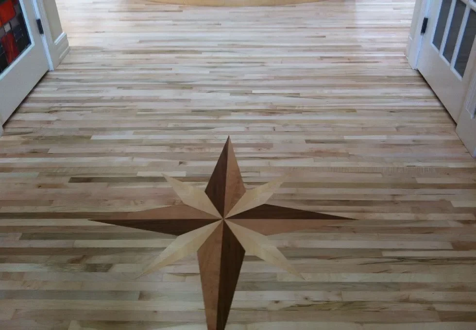 Custom hardwood flooring installation in a Calgary entryway featuring a precision-cut wood medallion compass rose inlay set within light toned maple planks