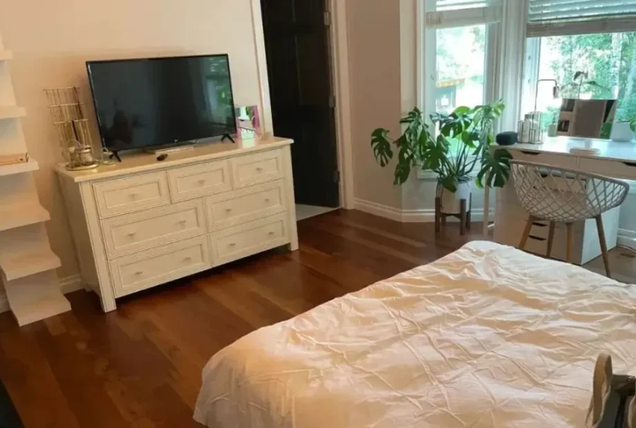 A beautifully finished bedroom featuring rich, dark wood floors installed by a professional hardwood flooring contractor, showing seamless transitions against white baseboards and modern furniture